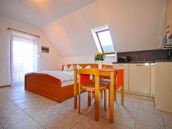 A bedroom with a bed, a desk, and a chair. There is a window with curtains and a small table with a vase.