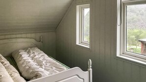 Et soveværelse med en enkeltseng, to vinduer og udsigt til grønne omgivelser.