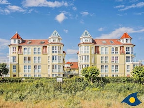 A yellow building with multiple windows and red roofs, surrounded by greenery.