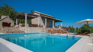 A poolside area with a stone building, lounge chairs, and a pergola.