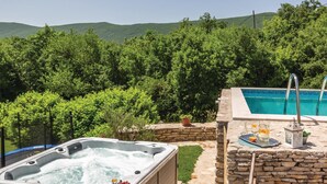 A hot tub with a stone wall and a pool with a stone deck.
