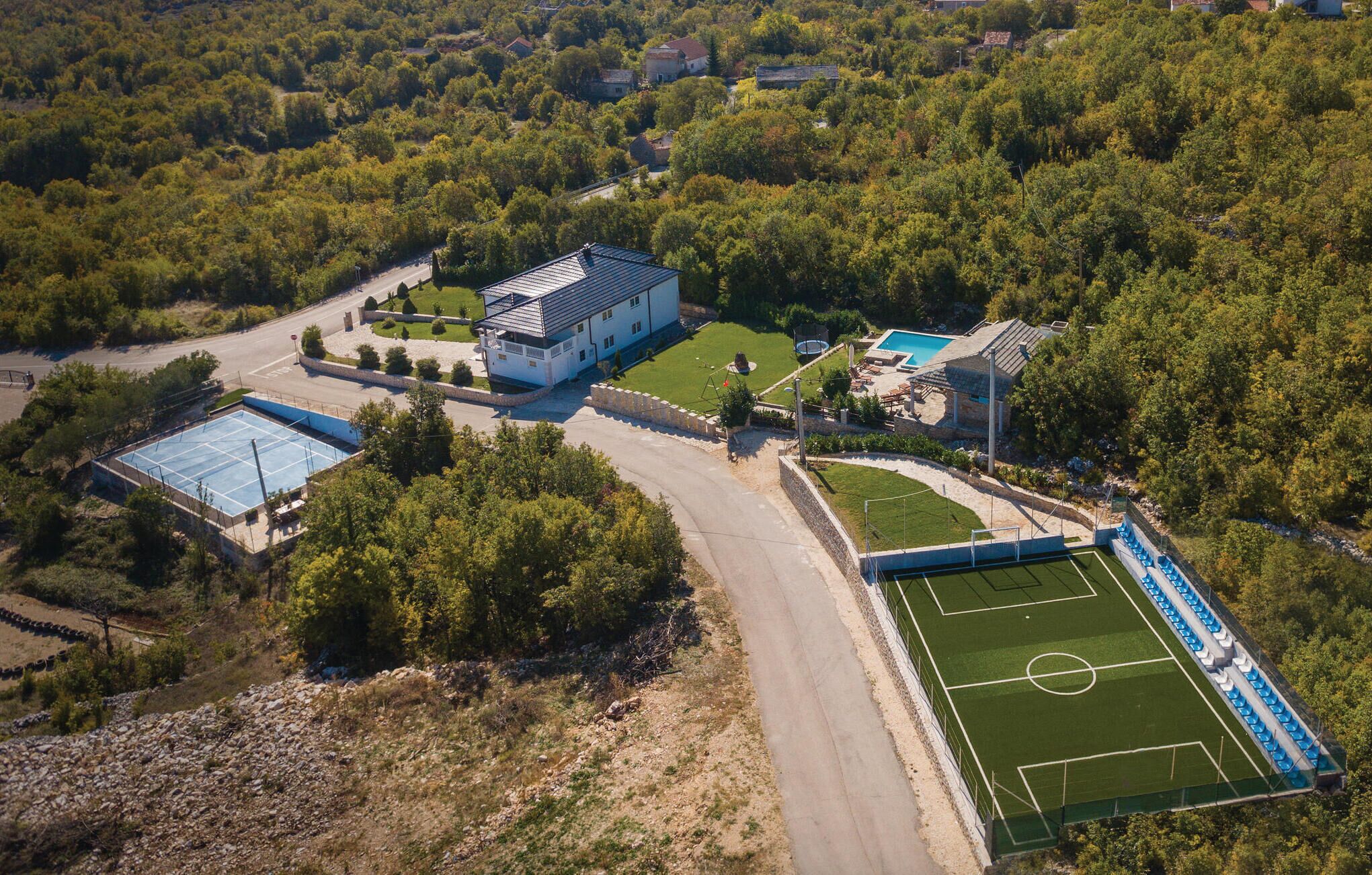An aerial view of a residential area with a large house, tennis courts, and a swimming pool.