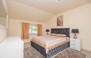 A bedroom with a large bed, two bedside tables, a dresser, a window with curtains, and a painting on the wall.
