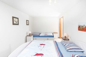 Une chambre avec deux lits, des murs blancs et des tableaux encadrés.