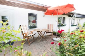 Une terrasse extérieure avec une table et des chaises en bois, un parasol rouge et des plantes en pot.