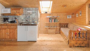 A cozy cabin interior with a wooden floor, a kitchenette with a microwave, a dining table, and a sofa. - Ferienhaus Klein St. Paul (Klein St. Paul)