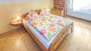 A wooden bed with floral bedding, a nightstand with a lamp, and a brick wall in the background. - Ferienhaus Klein St. Paul (Klein St. Paul)