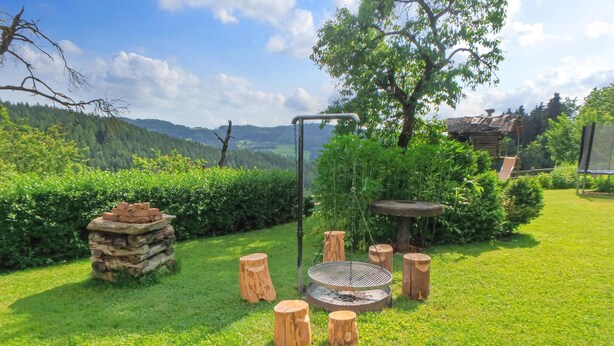 A well-maintained garden with a fire pit, wooden stools, and a stone stack. - Ferienhaus Klein St. Paul (Klein St. Paul)
