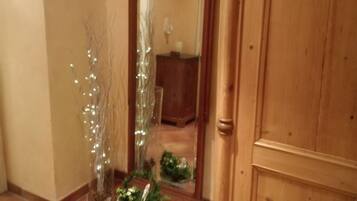 Ein Flur mit einer Holztür, einem Spiegel, der einen Raum reflektiert, und einem Blumentopf mit Beleuchtung.