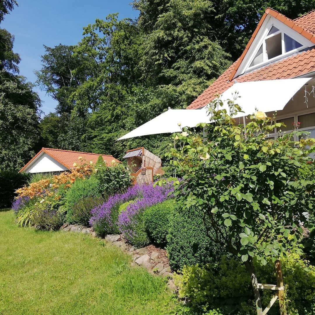 Ein Haus mit rotem Ziegeldach, umgeben von üppiger Vegetation und blühenden Pflanzen.