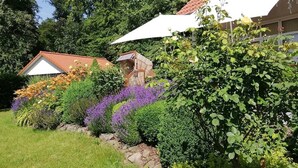 Uma casa com telhado de telhas vermelhas, rodeada por vegetação exuberante e plantas floridas.