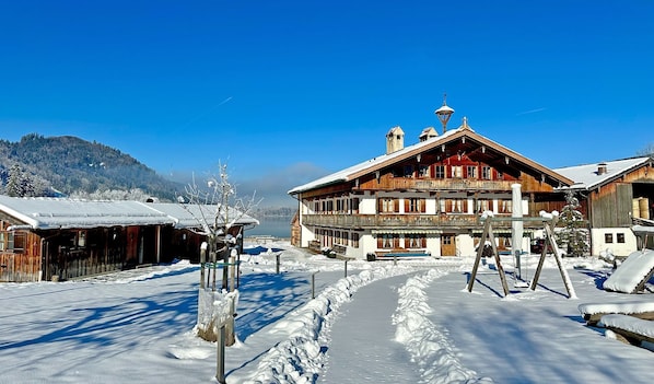 A traditional wooden building with a balcony, a snow-covered path, and a mountain in the background.