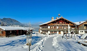 A traditional wooden building with a balcony, a snow-covered path, and a mountain in the background.