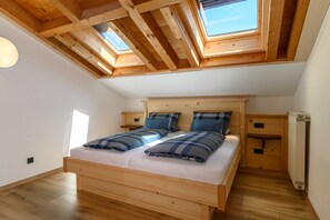 Un dormitorio con cama de madera, tragaluces, radiador y una mesita de noche.