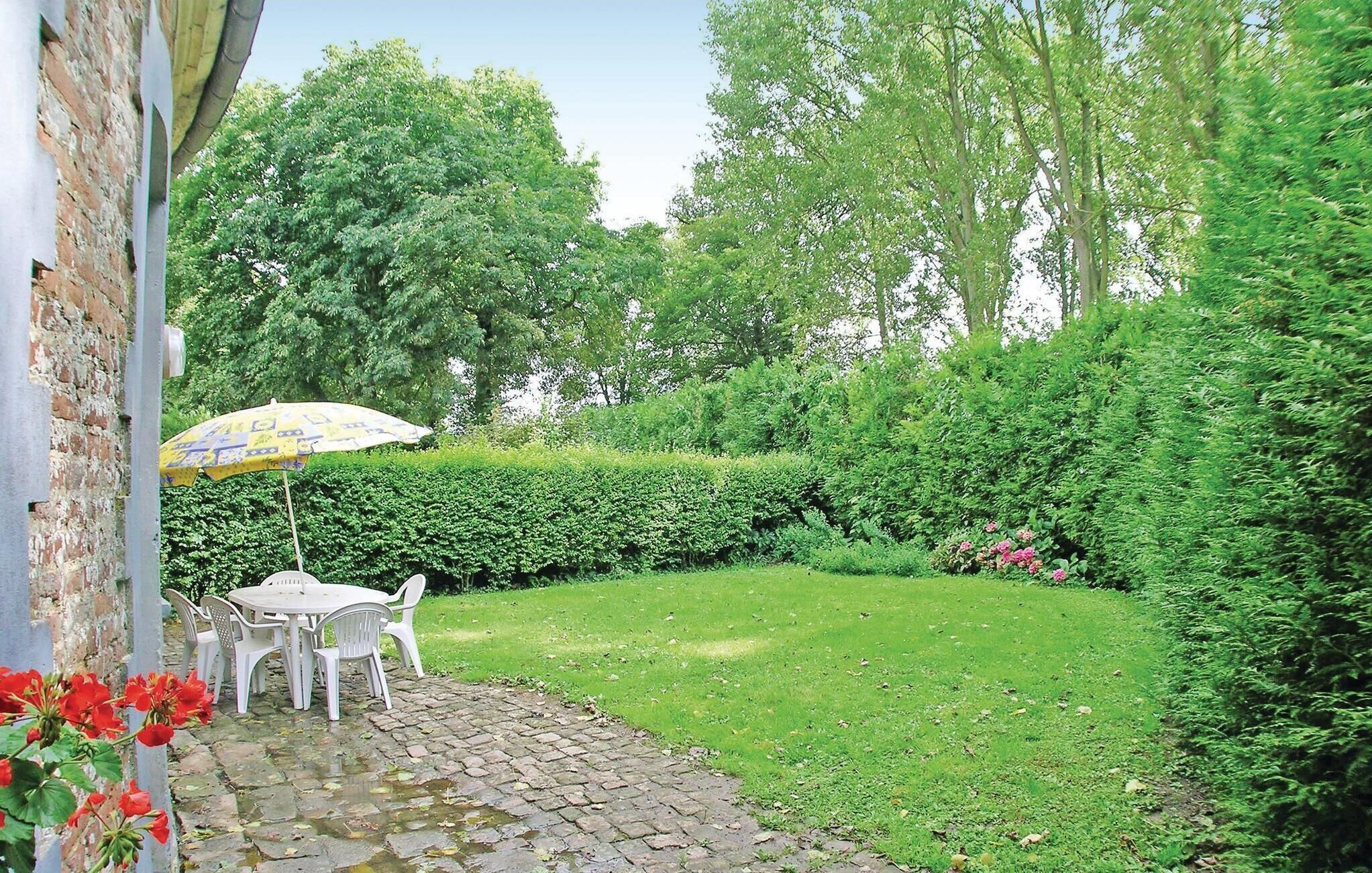 A garden with a paved patio, a table with chairs, and a yellow umbrella.