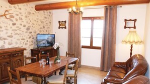 A cozy living room with a wooden dining table, chairs, a leather sofa, a television, and a decorative lamp. - 2 bedroom gorgeous home in Sigoyer (Sigoyer)