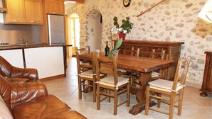 A dining area with a wooden table and chairs, a leather sofa, and a kitchen in the background. - 2 bedroom gorgeous home in Sigoyer (Sigoyer)