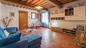 A living room with a blue sofa, wooden beams on the ceiling, a television, and a bookshelf with decorative items. - Stunning apartment in Buti (PI) with swimming pool (Buti (PI))