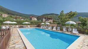 A swimming pool with lounge chairs and umbrellas, surrounded by stone walls and a wooden fence, with a mountainous backdrop. - Stunning apartment in Buti (PI) with swimming pool (Buti (PI))
