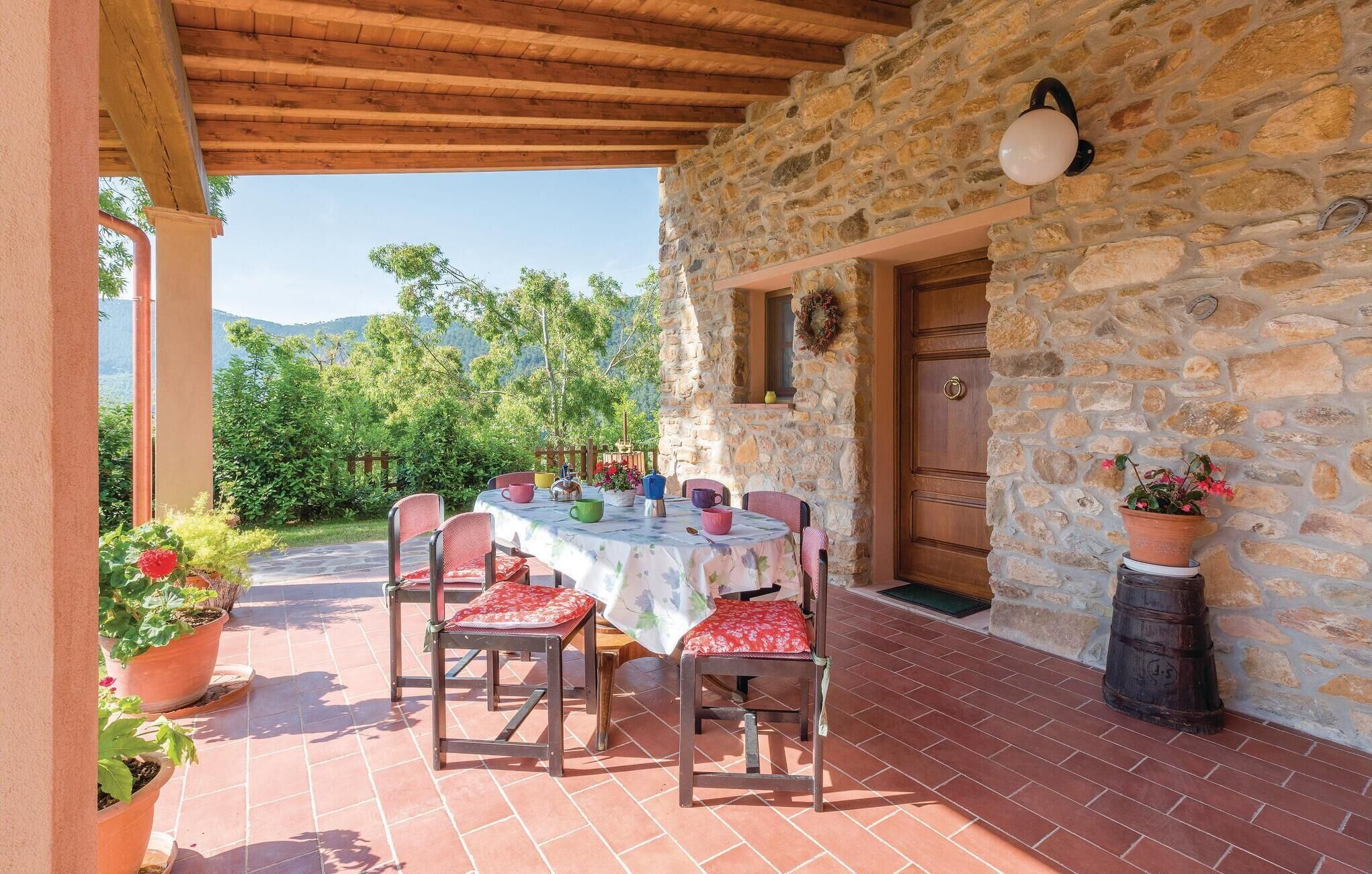 A covered outdoor dining area with a stone wall, wooden ceiling, and a view of greenery and hills.