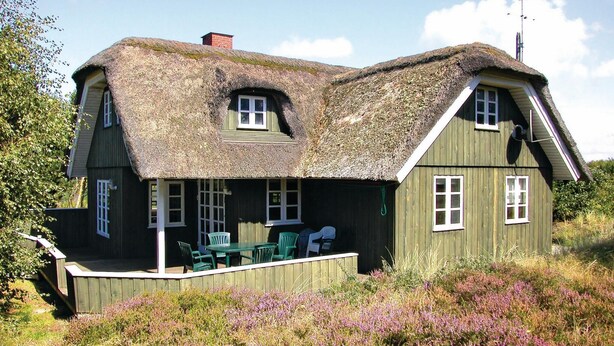Een woonhuis met twee verdiepingen, een rieten dak, een houten terras en een klein zitgedeelte buiten.