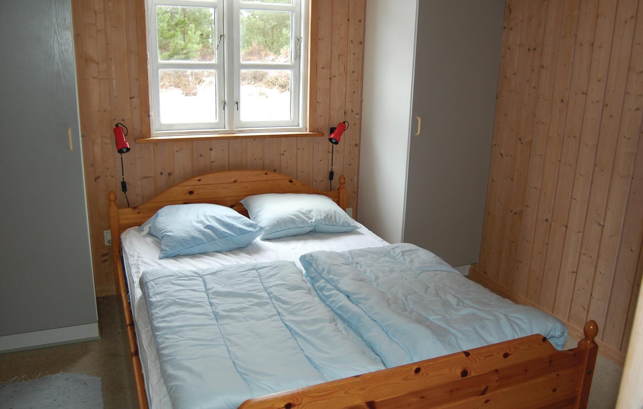 Una cama de madera con cabecera, dos almohadas y una manta en una habitación con paredes de madera y una ventana.