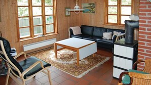 Een gezellige woonkamer met een zwarte leren bank, een houten salontafel, een rieten fauteuil en een open haard.