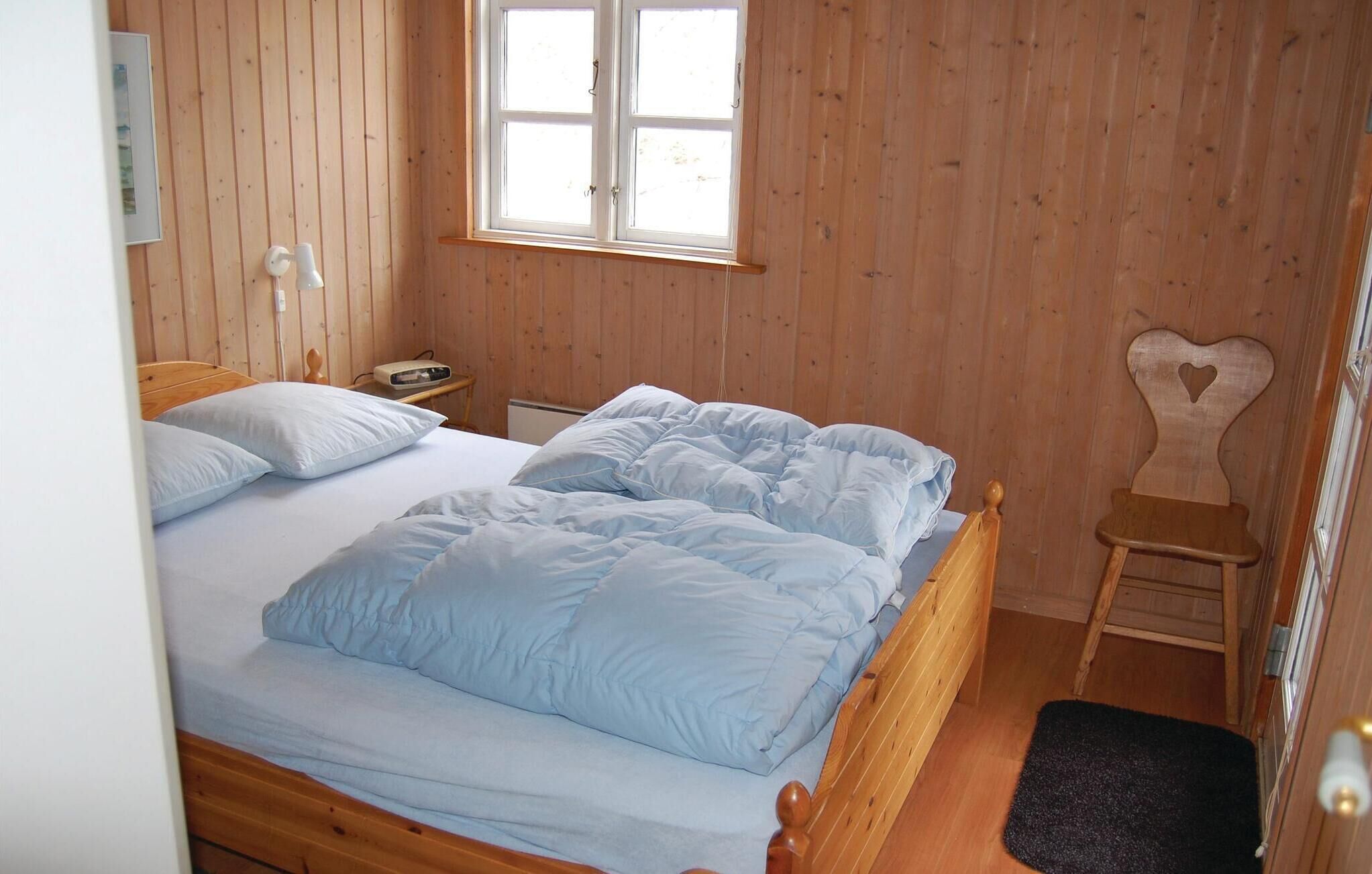 Een kamer met houten lambrisering, een bed, een nachtkastje, een heater en een stoel in de vorm van een hart.