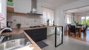 Una cucina moderna con piano cottura a gas, mobili neri e piano di lavoro in legno. C'è una zona pranzo con tavolo e sedie, e vista sul verde circostante.