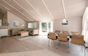 A spacious room with a high ceiling, wooden walls, a dining table with chairs, a sofa, and a kitchen area. - 3 bedroom awesome home in Nexø (Nexø)