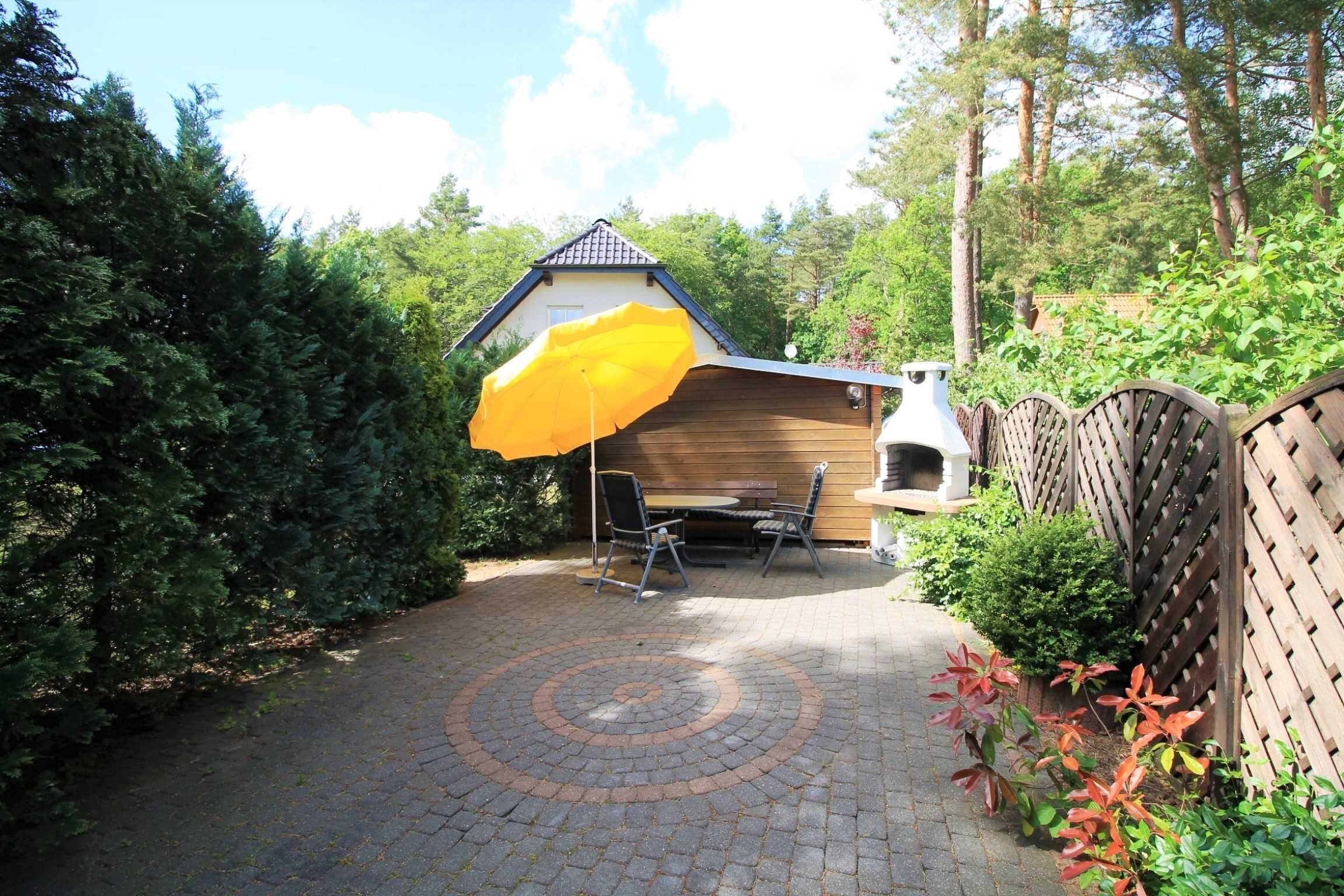A patio area with a wooden table and chairs, a yellow umbrella, and a brick pathway.