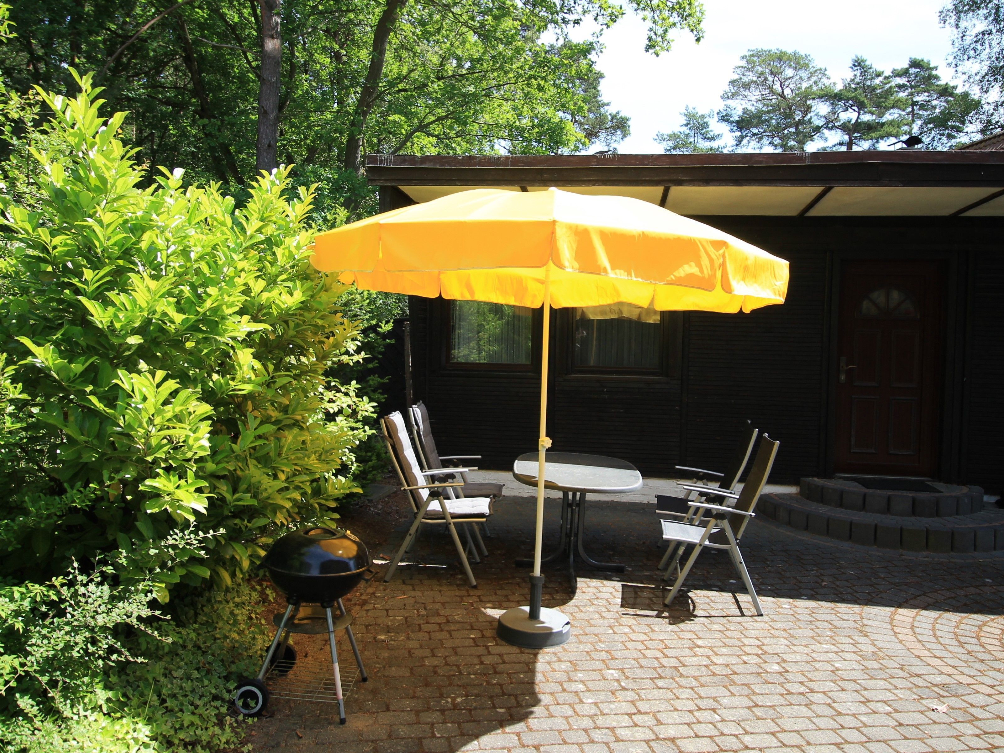 An outdoor patio with a brick floor, a yellow umbrella, and a grill.