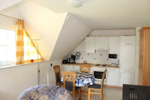 A compact kitchen with white cabinets, a dining table with chairs, and a window with curtains.
