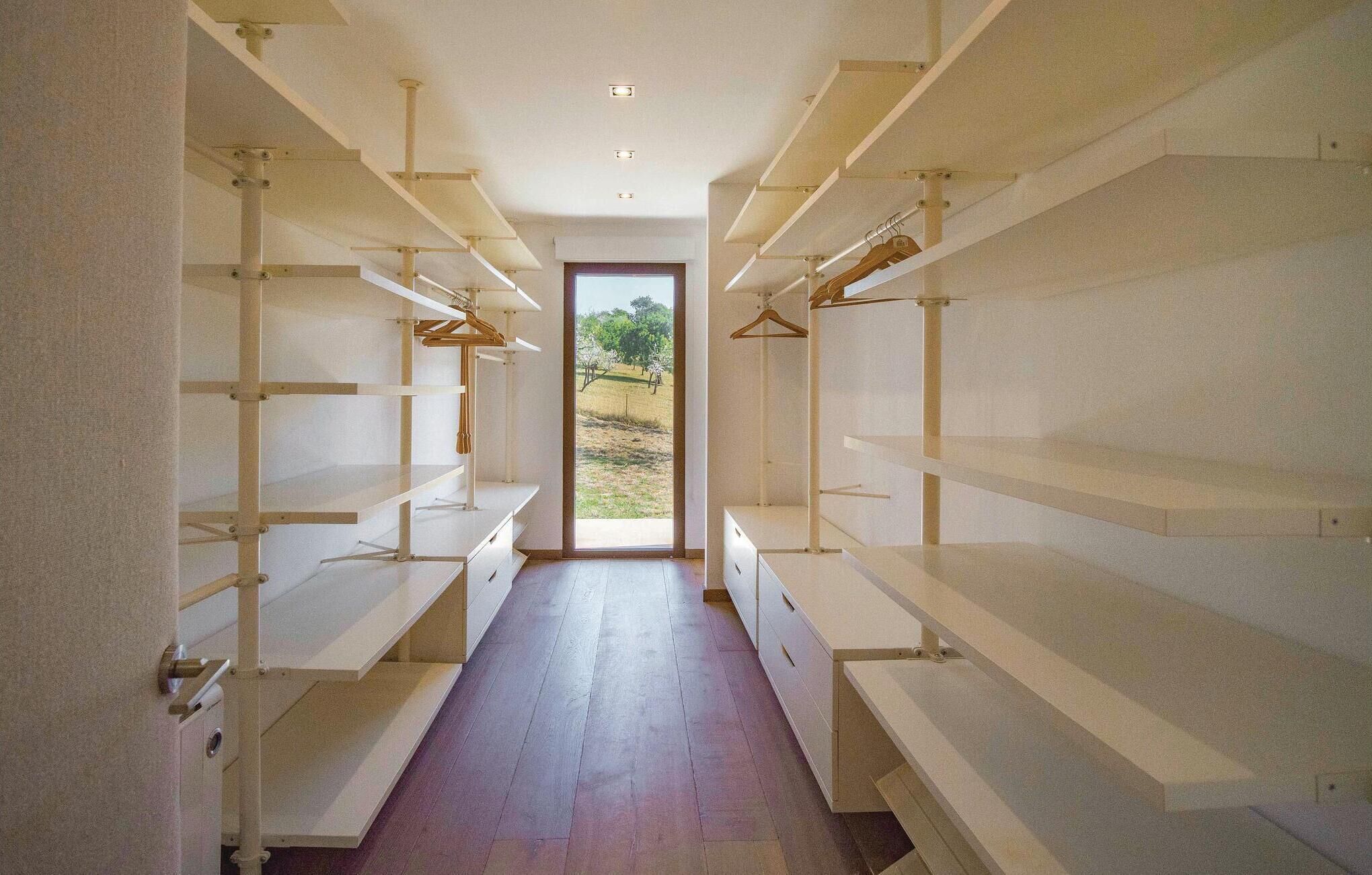 A narrow hallway with open shelving units on both sides, leading to a door with a view of an outdoor area.