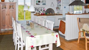 A dining area with a table set for four, white chairs, a wooden cabinet, and a kitchen area with white cabinets and a window. - Amazing home in Rømø with WiFi (Rømø)