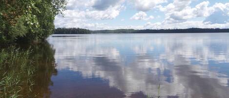 A calm lake with clear reflections of the sky and surrounding trees.