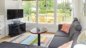 A living room with a grey sofa, a TV, a small table, and a view of a garden through large windows. - Nice home in Långaryd with WiFi (Långaryd)