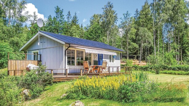 A cabin with a covered porch, a deck, and a view of a forested area. - Nice home in Långaryd with WiFi (Långaryd)