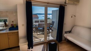 Eine kompakte Küche mit Essbereich, einer Couch und einer Glasschiebetür, die auf einen Balkon mit Meerblick führt.