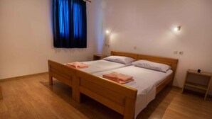 Ein Doppelbett mit Holz-Kopf- und Fußteil, zwei Nachttische, ein kleiner Beistelltisch und ein Fenster mit blauen Vorhängen.