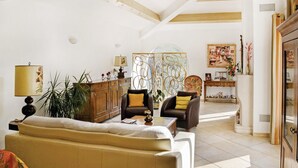 Un salon spacieux doté d’un haut plafond, de poutres apparentes, d’un grand canapé, de deux fauteuils, d’une table basse et d’une cloison décorative.