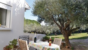 Une terrasse extérieure avec une table dressée pour deux personnes, entourée d’oliviers et bordée d’un bâtiment blanc.