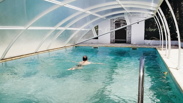 Une piscine intérieure dotée d’un plafond en verre transparent et d’un mur en pierre en arrière-plan.