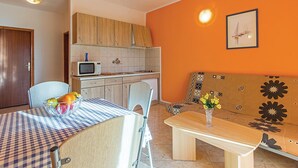 Cocina compacta con microondas, estufa y armarios de madera. En primer plano, una mesa de comedor con sillas y un jarrón con flores.