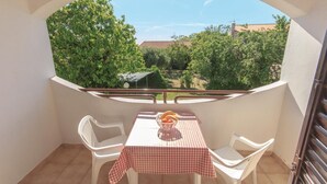 Un balcón con una mesa y sillas, un mantel a cuadros y un cuenco de fruta.