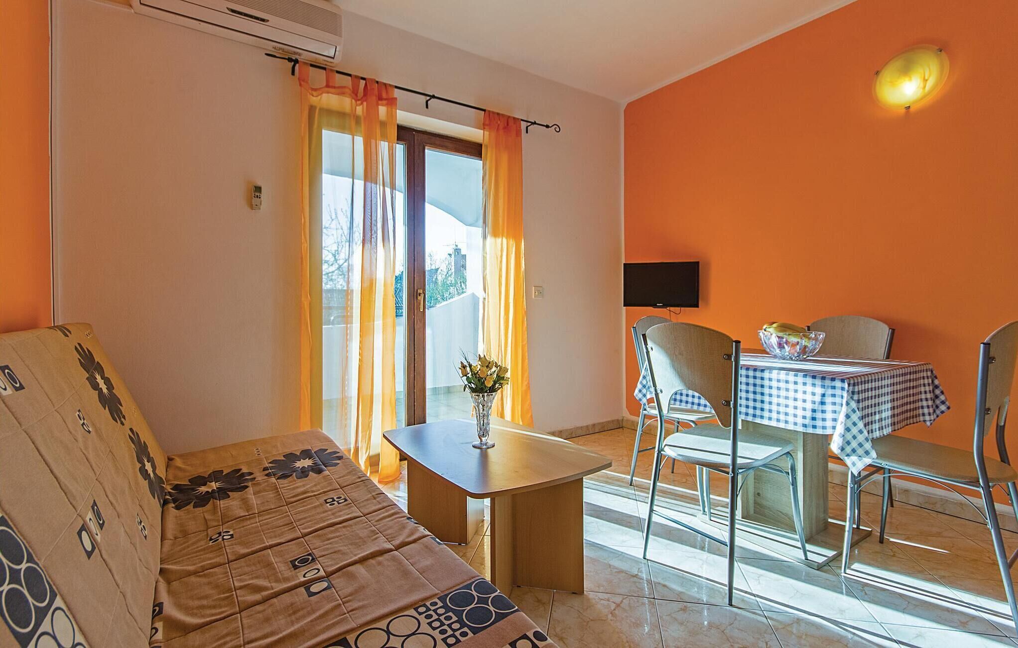 A room with a sofa, a small table with a vase, and a dining area with chairs and a table.