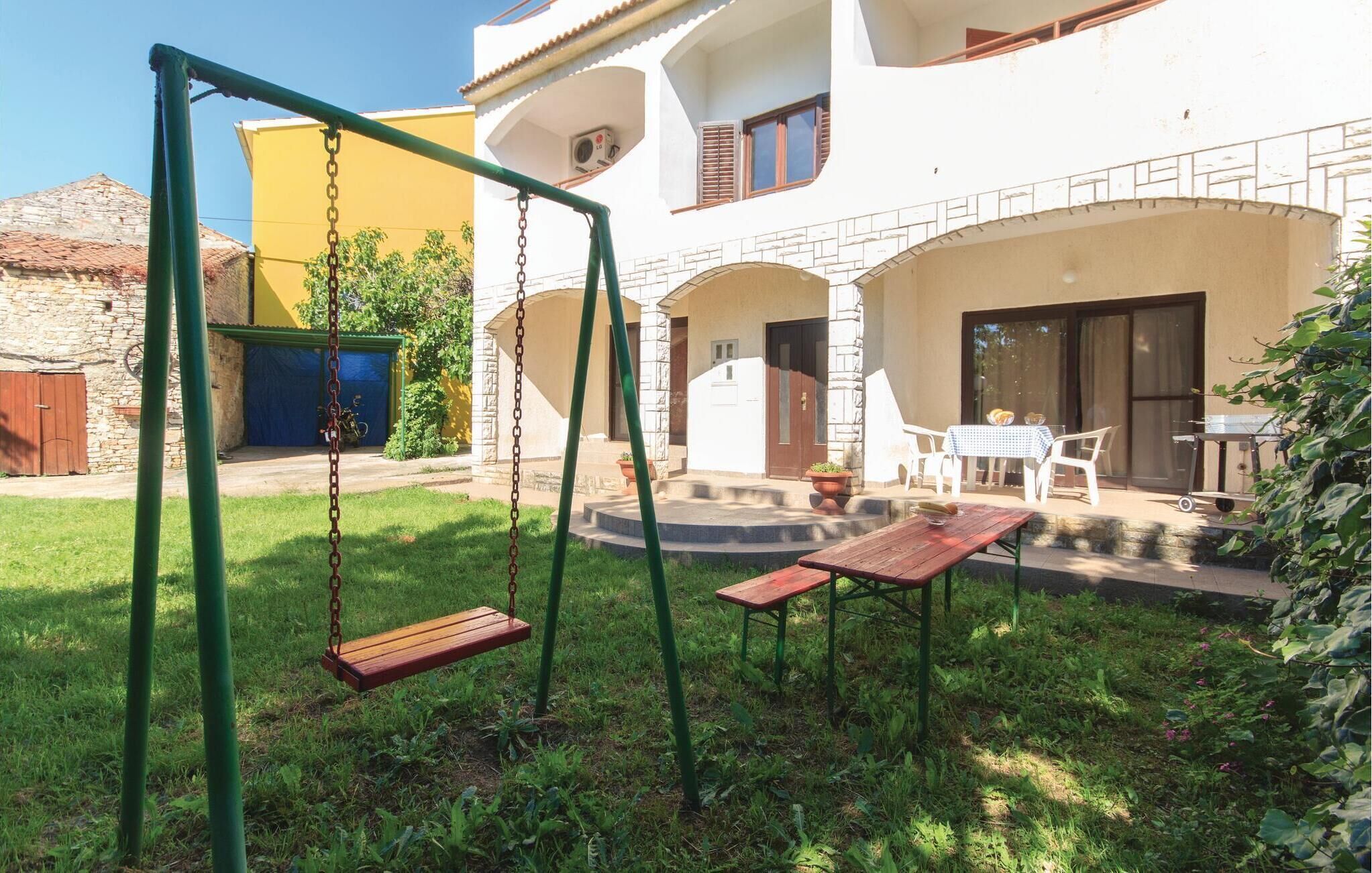 A patio area with a swing set, a table with chairs, and a view of a building with stone walls and a yellow facade.