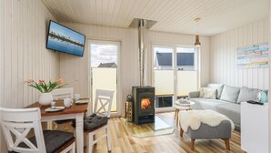 A cozy room with a wooden floor, a white sofa, a dining table with chairs, a TV mounted on the wall, and a fireplace. - Lovely home in OstseeResort Olpenitz with sauna (OstseeResort Olpenitz)