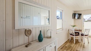 A room with a large mirror, a wooden console table with decorative items, a television mounted on the wall, and a dining area with chairs and a table. - Lovely home in OstseeResort Olpenitz with sauna (OstseeResort Olpenitz)