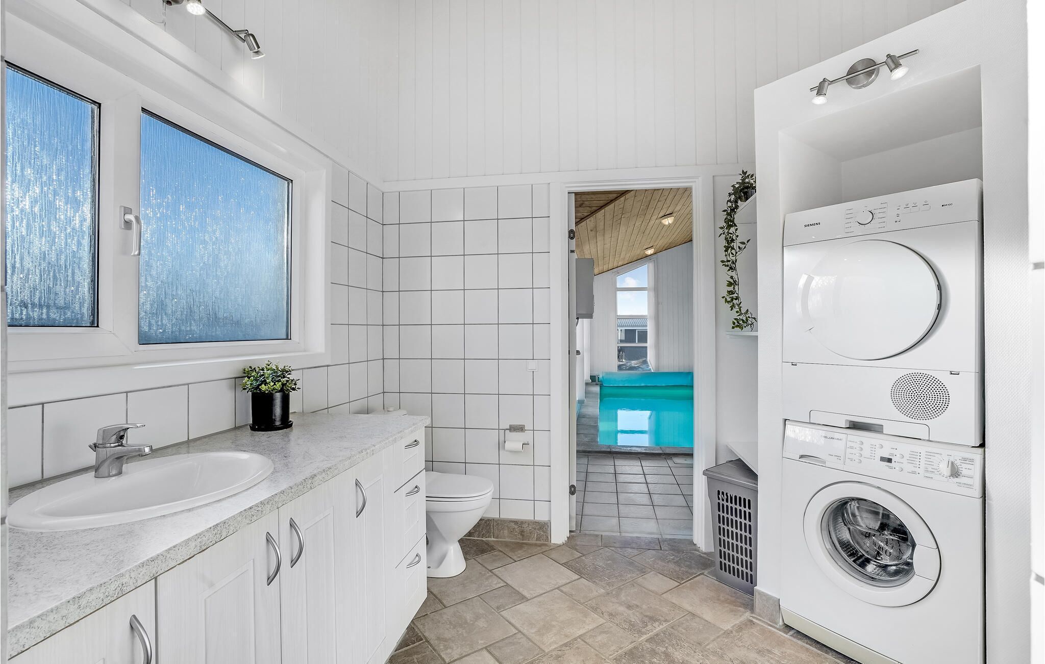 Ein kleines, modernes Badezimmer mit Waschbecken, Toilette und gestapelter Wascher-Trockner-Kombination.